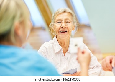 Happy Elderly Woman In Assisted Living Playing Cards With A Caregiver