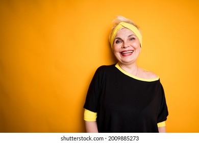 Happy Elderly Woman In Black T-shirt Smiling Broadly While Standing On Yellow Background