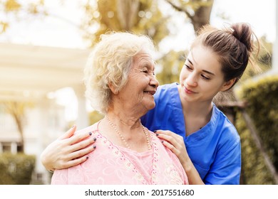 Happy Elderly Woman With A Caregiver In The Garden, Senior Woman With Nurse Or Doctor. Home Care Concept.