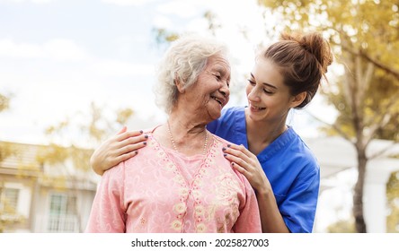 Happy Elderly Woman With A Caregiver In The Garden, Senior Woman With Nurse Or Doctor. Home Care Concept.