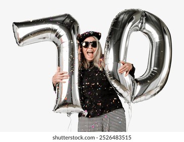 Happy elderly woman celebrating 70th birthday with large silver balloons. Elderly woman wearing sunglasses, confetti, and hat. 70th birthday joy for elderly woman. 70 with balloons, isolated on white. - Powered by Shutterstock