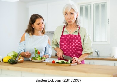 Happy Elderly Woman And Her Adult Daughter Making Dinner Together In Kitchen