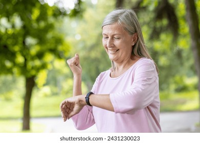 Happy elderly woman monitoring her exercise on a smartwatch, enjoying a healthy lifestyle in a natural outdoor setting. - Powered by Shutterstock