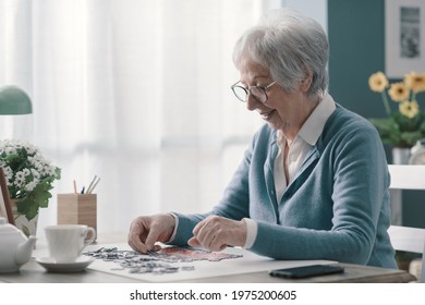 Happy elderly woman relaxing at home alone, she is solving a puzzle and drinking tea