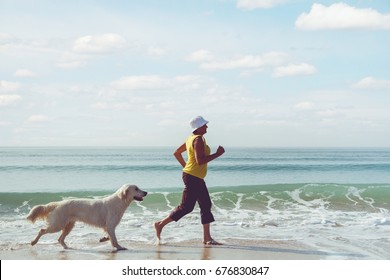 Happy elderly woman running along a beach with her golden retriever at the morning - Powered by Shutterstock