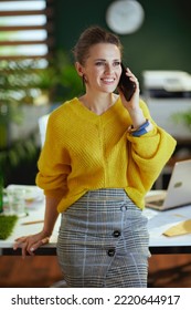 Happy Elegant 40 Years Old Small Business Owner Woman In Yellow Sweater In The Modern Green Office Talking On A Smartphone.