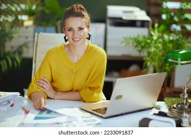 happy elegant 40 years old small business owner woman in yellow sweater with laptop working with documents in the modern green office. - Shutterstock ID 2233091837