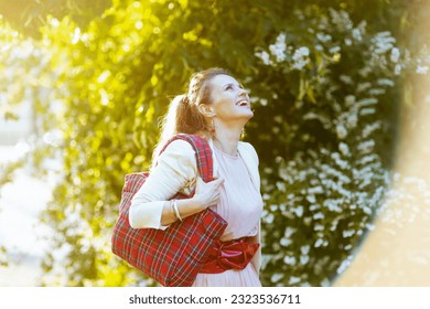 happy elegant 40 years old woman in pink dress and white jacket in the city with red bag.