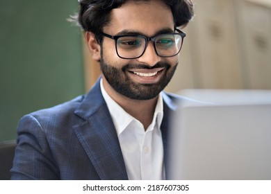 Happy Elegant Indian Young Business Man Executive Professional Manager, Office Employee Worker Wearing Suit And Eyeglasses Working Online On Laptop Looking At Pc Computer Corporate Data Technology.