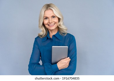 Happy Elegant Middle Aged Older Professional Business Woman Leader, Consultant Manager, Looking At Camera Holding Digital Tablet Isolated On Grey Wall Advertising Corporate Online E Learning Webinars.