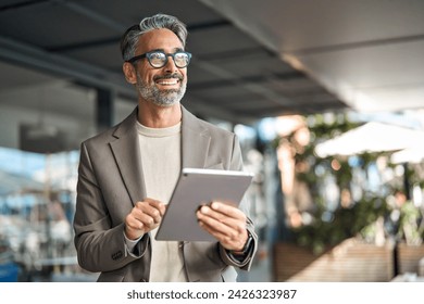 Happy elegant middle aged professional business man financial executive manager using digital tablet. Smiling confident mature businessman holding tab computer technology looking away at copy space. - Powered by Shutterstock