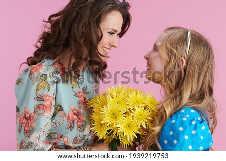 happy elegant mother and daughter with long wavy hair presenting yellow chrysanthemums flowers against pink background.