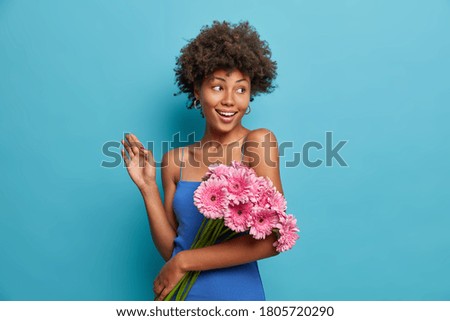 Happy elegant nice woman with bouquet of pink gerbera daisy, gets flowers from boyfriend on date, has good mood as received pleasant birthday gift isolated blue background. Flowers delivery service
