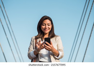 A happy elegant young woman stands and uses her phone to type an important message. A businesswoman using technologies outdoors.