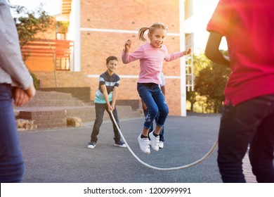 Happy elementary kids playing together with jumping rope outdoor. Children playing skipping rope jumping game and laughing outdoors. Happy cute girl jumping over skipping rope held by her friends.