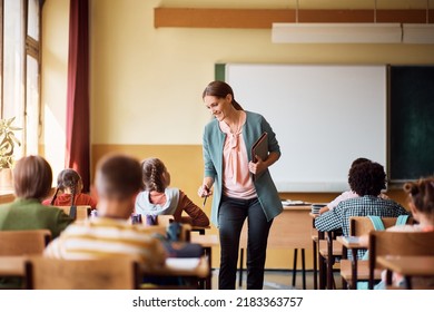 Happy elementary school teacher assisting her student in the classroom.  - Shutterstock ID 2183363757