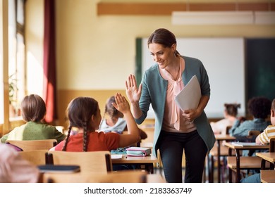 Happy elementary school teacher giving high-five to her student during class in the classroom.