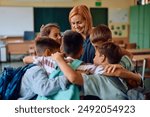 Happy elementary school teacher and her students embracing while greeting on first day of school. 