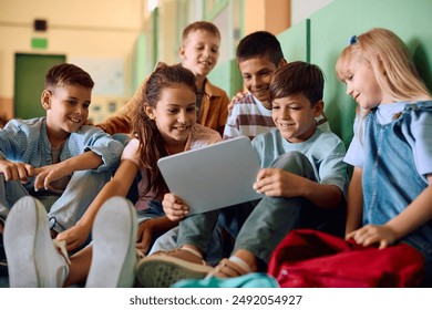 Happy elementary students surfing the net on touchpad while relaxing in a hallway. - Powered by Shutterstock