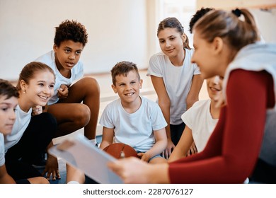 Happy elementary students and their basketball coach going through exercise plan during physical activity class at school. - Powered by Shutterstock