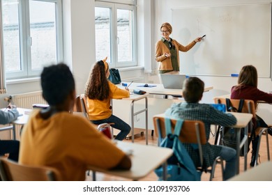 Happy Elementary Teacher Explaining Math Lesson On Whiteboard To Her Students During A Class. 