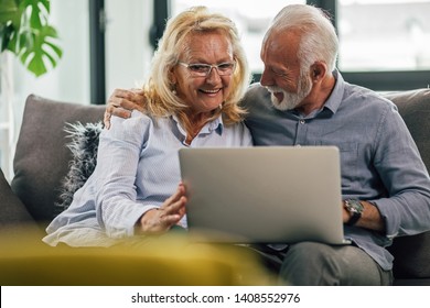 Happy Embraced Mature Couple Relaxing On The Sofa At Home And Surfing The Net On A Computer. 