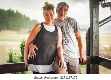 Happy Embracing Couple, Generation X, Posing, Leaning Against A Fence, In Rainy Weather On The Beautiful Green Hills Of The Mountain