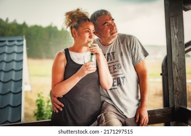 Happy Embracing Couple, Generation X, Posing Glass Of Drink With A Straw, Leaning Against A Fence, In Rainy Weather On The Beautiful Green Hills Of The Mountain