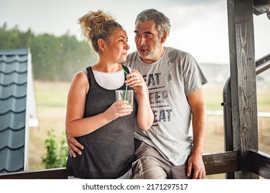 Happy Embracing Couple, Generation X, Posing Glass Of Drink With A Straw, Leaning Against A Fence, In Rainy Weather On The Beautiful Green Hills Of The Mountain