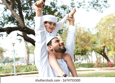 Happy Emirati father with son both on Kandora. Arab dad with young boy kid spending time together. Arabic man on dish dash with his child
