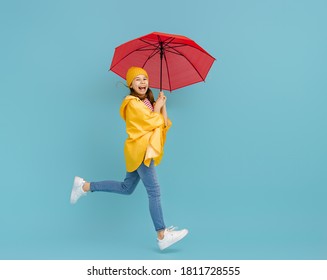 Happy Emotional Child Laughing And Jumping. Kid With Red Umbrella On Colored Teal Background.