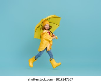 Happy Emotional Child Laughing And Jumping. Kid With Yellow Umbrella On Colored Teal Background.