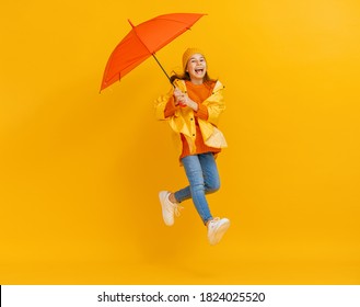 Happy Emotional Child Laughing And Jumping. Kid With Orange Umbrella On Colored Red Background.