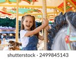 Happy emotional child riding on a merry go round at amusement park. Little girl playing on carousel, summer fun, happy childhood, vacation and entertainment concept