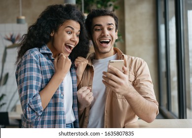 Happy Emotional Couple Celebration Success. Excited Friends Using Smartphone, Playing Video Games. Portrait Of Overjoyed Online Lottery Winners Holding Mobile Phone, Looking At Digital Screen