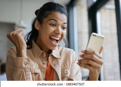 Happy Emotional Girl Celebrates Victory, Sports Betting Concept. Young Excited African American Woman Using Mobile App For Online Shopping With Cash Back