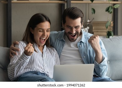 Happy emotional positive young family couple woman man looking at computer screen, celebrating online lottery giveaway betting auction win, feeling overjoyed together at home, internet success concept