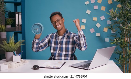 Happy employee checking time on clock and finishing work before deadline, doing countdown for timeout. Punctual man feeling cheerful about break timing, looking at watch with hour and minutes.