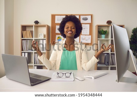 Happy employee getting ready to start productive work day. Young business woman sitting at office desk and meditating eyes closed thinking of good things and focusing on positive feelings and emotions