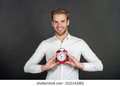 Happy employee holding alarm timepiece dark background, clock