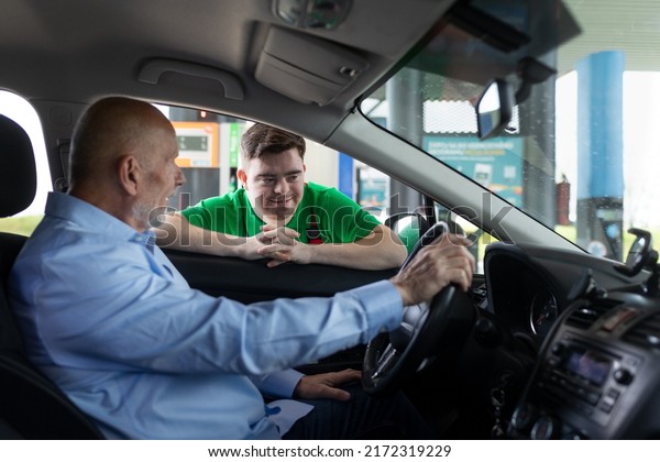 Happy employee man\
with Down syndrome talking with customer in car at gas station.\
Social inclusion concept.
