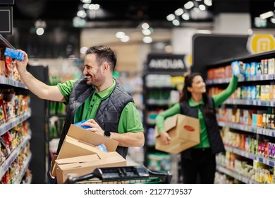 Happy employees putting groceries on shelves at supermarket. - Shutterstock ID 2127719537