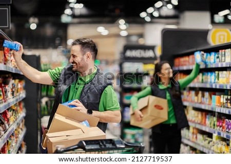 Happy employees putting groceries on shelves at supermarket.