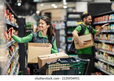 Happy employees putting products on shelves in supermarket.