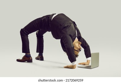 Happy energetic businessman practises yoga positions while working on laptop computer. Funny fit flexible young man in suit and glasses doing bridge pose on studio floor while using modern notebook PC - Shutterstock ID 2172069259