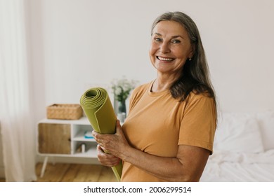 Happy energetic middle-aged woman getting ready on sports training. Cheerful woman holding sports mat and looking at camera with happiness. Yoga, meditation, sport and healthy lifestyle idea - Powered by Shutterstock