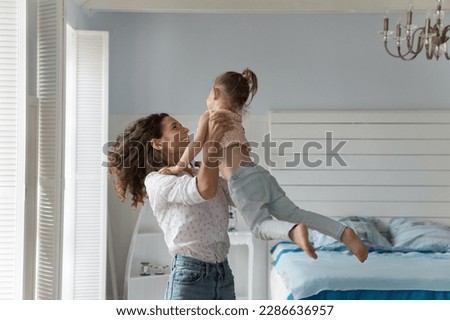 Happy energetic mother playing active games with little kid at home, lifting girl up in air, smiling, laughing, enjoying motherhood, family activity, leisure, having fun, dancing