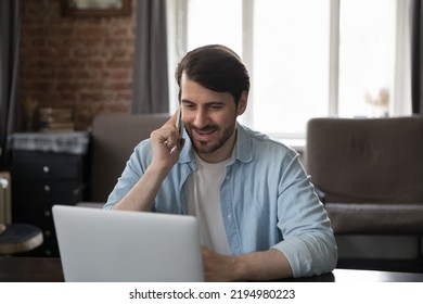 Happy Engaged Millennial Freelance Employee Man Answering Cellphone Call In Home Office, Talking To Client, Giving Phone Consultation To Customer On Mobile Phone, Working At Laptop Computer, Smiling