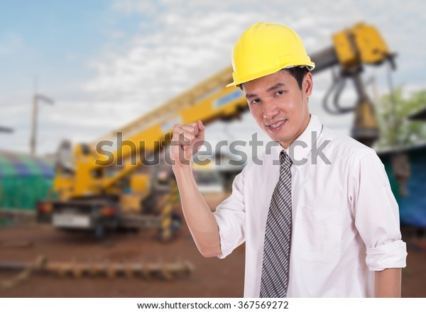 Happy engineer celebrating\
with arm raised, concept of successful, construction site\
background