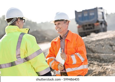 Happy engineer discussing with colleague at construction site on sunny day
